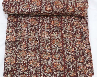 May include: A folded quilt featuring a deep maroon background with a repeating floral pattern in shades of orange, cream, and brown. The fabric displays visible running stitch details throughout, creating a textured surface across the entire textile.