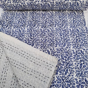 May include: A white cotton quilt with a blue floral pattern. The quilt is folded in half and the back side is visible, showing the stitching.