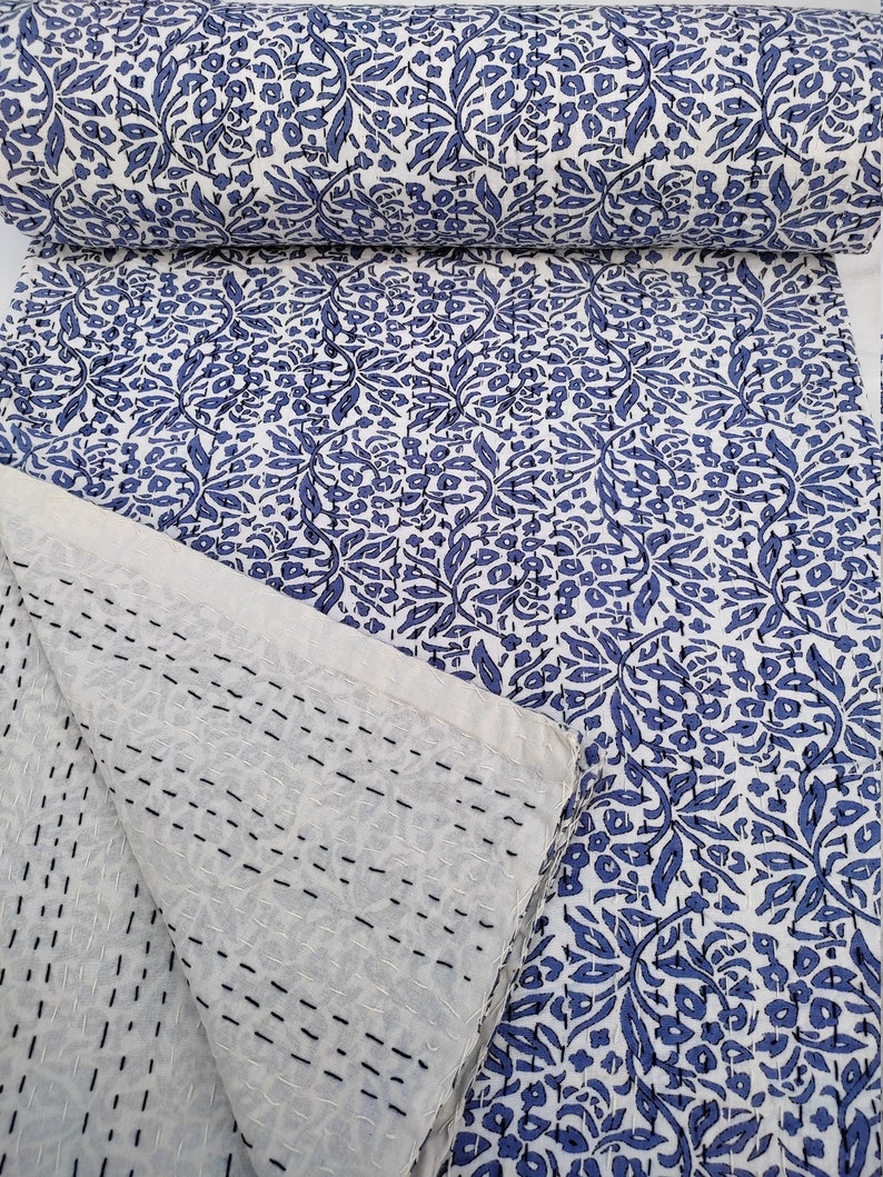 May include: A white cotton quilt with a blue floral pattern. The quilt is folded in half and the back side is visible, showing the stitching.