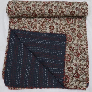 May include: A kantha quilt with a floral print in shades of brown and red on a cream background. The quilt is folded in half, revealing a dark blue underside with white stitching.
