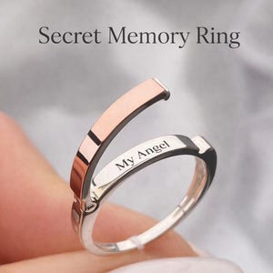 Pode incluir: Um anel Secret Memory prateado com um detalhe em ouro rosa. O anel tem as palavras "My Angel" gravadas no interior. A imagem também inclui o texto "Hidden engraving inside".
