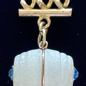 May include: A white glass bead with a gold band around the middle. The bead is attached to a gold chain with a gold clasp.