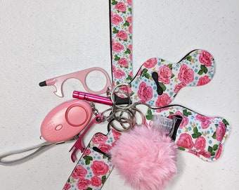 May include: A pink and white floral patterned keychain with a pink hand sanitizer holder, a pink personal alarm, a pink bottle opener, a pink and silver key ring, and a pink fuzzy pom-pom.