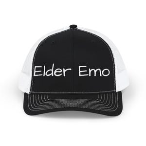 May include: A black and white trucker hat featuring a solid black front panel with the text Elder Emo embroidered in white. The cap includes a white mesh back, a black brim with white stitching, and a button on the top center of the crown.