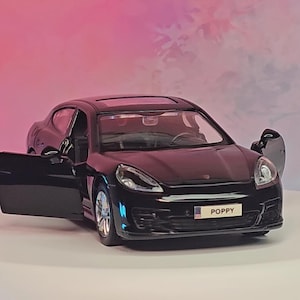 May include: A black model car with an open door, revealing interior details. The car has the word "POPPY" on the number plate. The image also includes the text "CarModels Garage" in a circle.