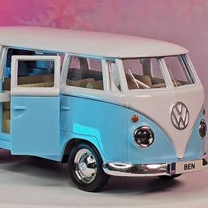 May include: A light blue and white Volkswagen Type 2 Bus model with the doors open. The model has chrome accents, a VW logo, and the name "BEN" on the front. The model is a collectible item.