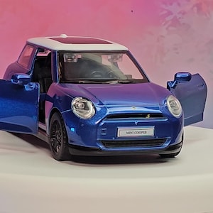 Könnte beinhalten: Ein blaues Mini Cooper Modellauto mit geöffneten Türen, das den Innenraum freigibt. Das Auto hat ein weißes Dach und schwarze Räder. Auf der Vorderseite des Autos steht der Text "MINI COOPER" auf einem kleinen Schild.