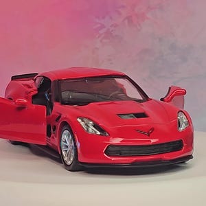 Puede incluir: Un coche de juguete rojo brillante con la puerta abierta, mostrando el interior. El coche tiene llantas plateadas y un diseño elegante. La imagen incluye el texto "CarModels Garage" en un círculo blanco.