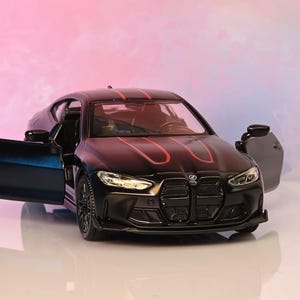 May include: A matte black scale model car featuring two prominent red racing stripes running along the hood and roof. The vehicle has open side doors, detailed headlights, a black front grille, and black wheels, capturing the design of a sports coupe.