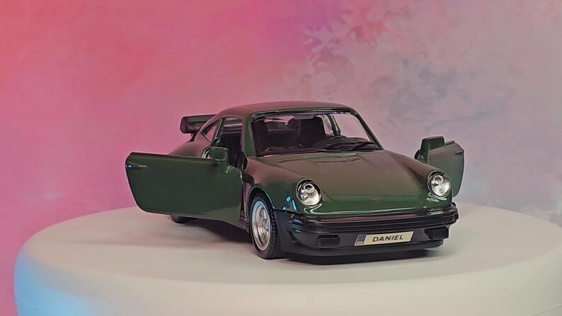 K&ouml;nnte beinhalten: Ein dunkelgr&uuml;nes Modellauto mit ge&ouml;ffneten T&uuml;ren, das den Innenraum zeigt. Das Auto hat eine schwarze Frontsto&szlig;stange und einen Heckspoiler. Der Name "DANIEL" ist vorne sichtbar.