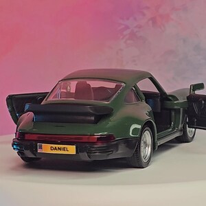 K&ouml;nnte beinhalten: Ein dunkelgr&uuml;nes Modellauto mit ge&ouml;ffneten T&uuml;ren, das einen roten Innenraum freilegt. Das Auto hat einen schwarzen Spoiler und silberne R&auml;der. Das Nummernschild lautet "DANIEL".