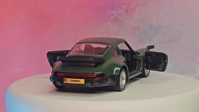 K&ouml;nnte beinhalten: Ein dunkelgr&uuml;nes Modellauto mit ge&ouml;ffneten T&uuml;ren, das einen roten Innenraum freilegt. Das Auto hat einen schwarzen Spoiler und silberne R&auml;der. Das Nummernschild lautet "DANIEL".
