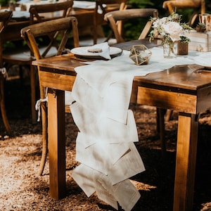 K&ouml;nnte beinhalten: Ein rustikaler Holztisch mit einer wei&szlig;en Tischdecke und einem Tischl&auml;ufer aus Buchseiten. Der Tisch ist mit einem Teller, einer Serviette und einer kleinen Glasvase mit Blumen gedeckt. In der Mitte des Tisches befindet sich ein geometrisches Glasornament.
