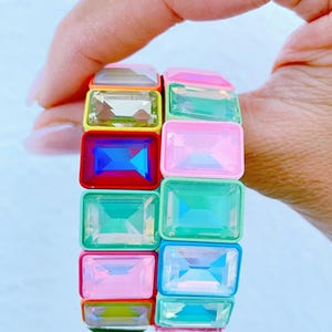 Op de afbeelding: Een kleurrijke armband met rechthoekige, edelsteenachtige kralen in verschillende kleuren, waaronder roze, groen, blauw, geel en transparant. De kralen zijn in een gestapeld ontwerp gerangschikt, waardoor een levendig accessoire ontstaat.
