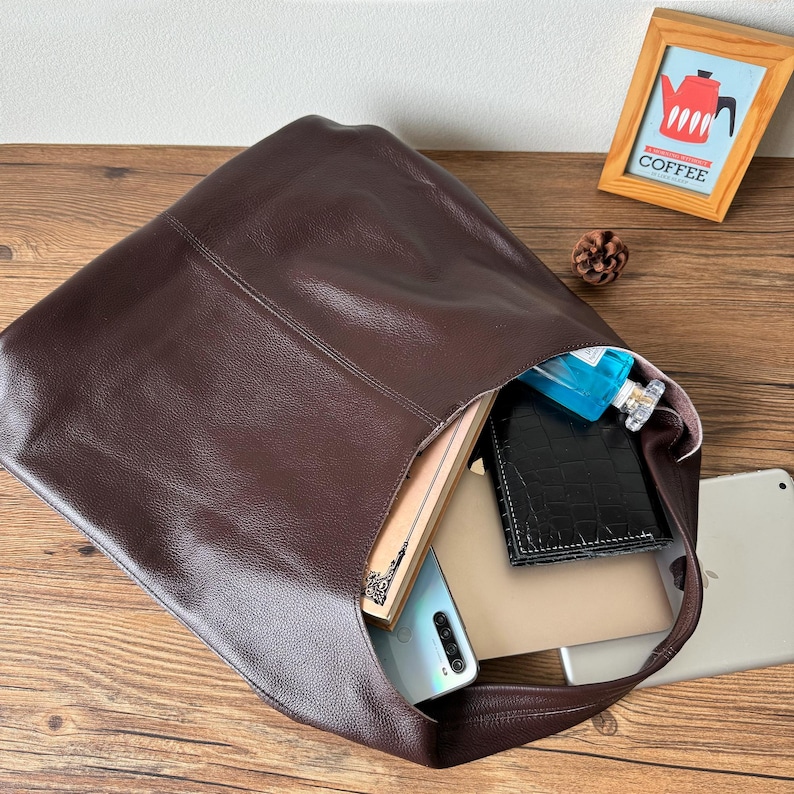 May include: A brown leather tote bag with a variety of items inside, including a book, a phone, a wallet, and a perfume bottle.
