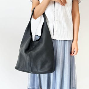 May include: A black leather tote bag with a slouchy design. The bag has a single strap and a wide opening.