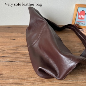 May include: A close-up of a brown leather tote bag. The bag is made of soft, supple leather and has a simple, classic design.