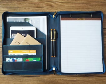 May include: A blue leather portfolio with a zipper closure, two pen holders, and multiple pockets. The portfolio has a notepad with the word "VERITAS" printed on the top. The portfolio also has a boarding pass and a few other papers inside.
