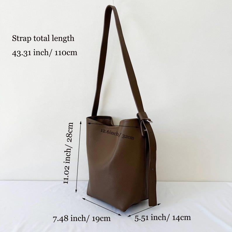 Puede incluir: Bolso de hombro de cuero marr&oacute;n con una correa larga. El bolso mide 28 cm de alto, 19 cm de ancho y 14 cm de profundidad. La correa mide 110 cm de largo. La abertura mide 32 cm de ancho. El texto indica la longitud total de la correa: 43,31 pulgadas/110 cm.
