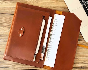 Könnte beinhalten: Eine braune Ledermappe mit Reißverschlusstasche und Knopfverschluss. Im Inneren befinden sich ein weißer Stift und mehrere Blätter Papier mit Text. Die Mappe ist geöffnet und zeigt ein gelbes Innenfutter und einen Laptop im Hintergrund.