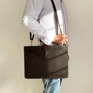 May include: A dark brown leather messenger bag with a shoulder strap and a buckle closure. The bag is rectangular and appears to be made of a distressed leather material. The strap is dark brown.