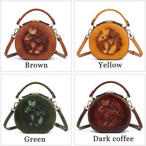 May include: Four round handbags in brown, yellow, green, and dark coffee. Each bag features a 3D embossed rabbit design and includes a top handle and a detachable shoulder strap. The colors are labeled: Brown, Yellow, Green, and Dark coffee.