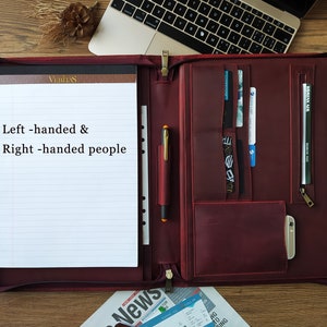 May include: A burgundy leather portfolio with a zippered closure and multiple pockets. The portfolio has a notepad with lined paper and the text "Left-handed & Right-handed people".