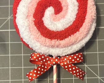May include: A red, white, and pink yarn lollipop with a red and white polka dot bow on a striped stick.
