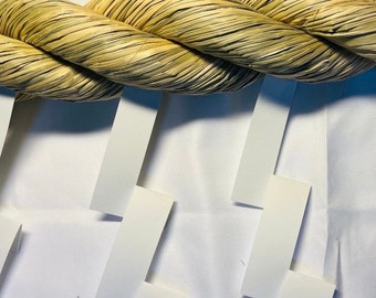 May include: A thick, woven rope made of natural fibers, with a light brown color, is hanging from a white surface. The rope is tied in a knot and has a rough texture.