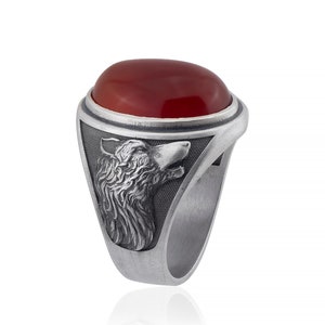 May include: A silver ring with a red carnelian stone and a wolf head design.