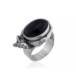 May include: A silver ring with a black oval gemstone and a detailed sculpted design of a ram's head on the side.