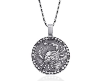 Op de afbeelding: Zilverkleurige hangerketting met een gedetailleerd krabontwerp in een cirkelvormig frame. De hanger hangt aan een bijpassende ketting. De krab is de centrale focus, met ingewikkelde details. De ketting is waarschijnlijk gemaakt van sterling zilver.