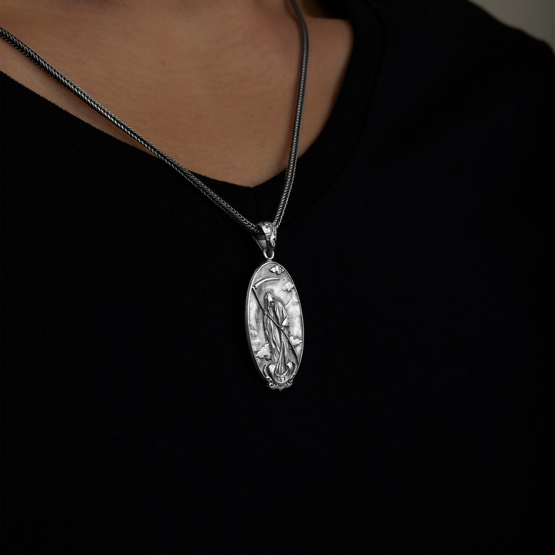 May include: A silver chain necklace with an oval pendant featuring a detailed depiction of the Grim Reaper holding a scythe.