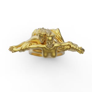 May include: A gold ring featuring a sculpted design of two figures intertwined. The figures are nude and appear to be embracing.