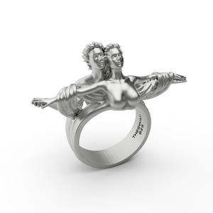 May include: A silver ring with a sculpted design of two figures embracing. The ring is marked "THESWAI 925".
