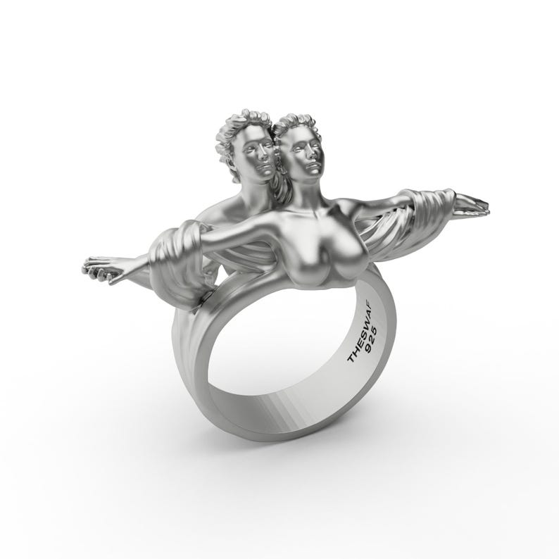 May include: A silver ring with a sculpted design of two figures embracing. The ring is marked "THESWAI 925".