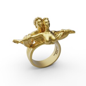 May include: A gold ring with a sculpted design of two figures embracing. The ring is inscribed with "THESWAI 925".
