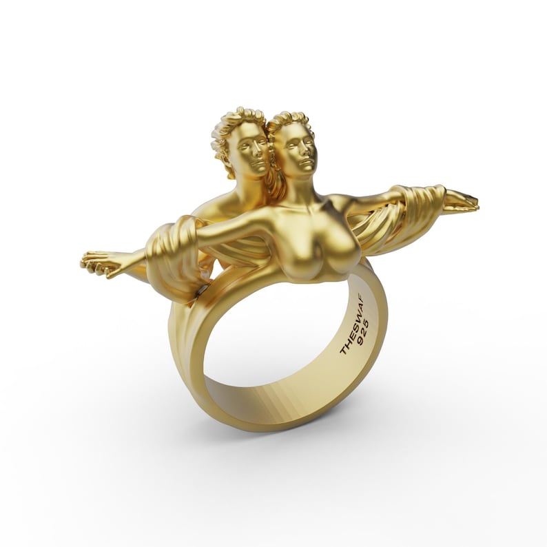 May include: A gold ring with a sculpted design of two figures embracing. The ring is inscribed with "THESWAI 925".