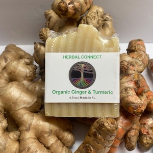 Puede incluir: Una pastilla de jabón con el texto "HERBAL CONNECT" y "Organic Ginger & Turmeric" en una etiqueta blanca. El jabón está rodeado de raíces frescas de jengibre y cúrcuma. El jabón pesa 128 gramos.