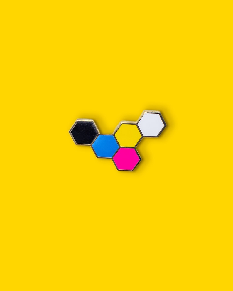 May include: A colorful enamel pin in a honeycomb design, featuring black, blue, yellow, pink, and white hexagonal shapes with silver trim. The pin is set against a bright yellow background.