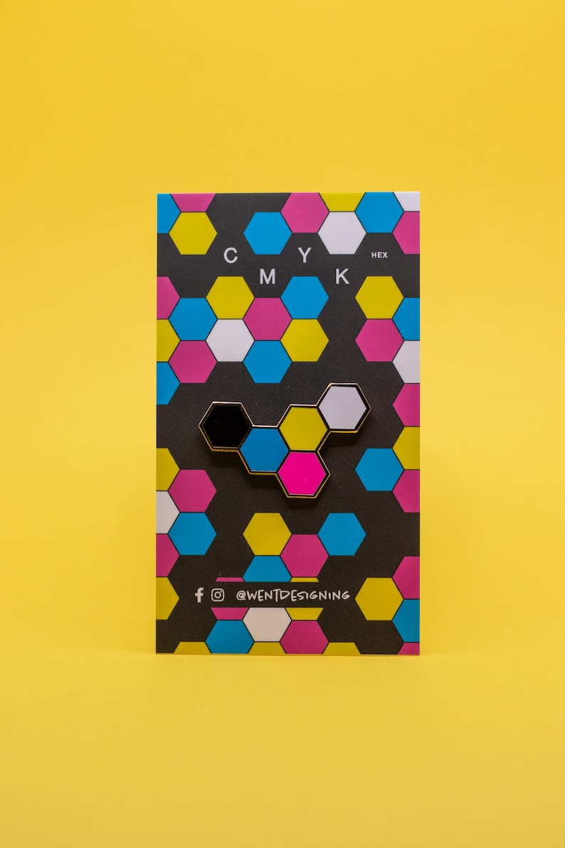 May include: A colorful enamel pin in a honeycomb design, featuring black, white, pink, blue, and yellow hexagons. The pin is on a black card with a repeating pattern of the same colors and the letters "CMYK" at the top.