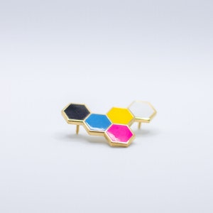 May include: A gold-toned pin with a honeycomb design. Each hexagon is a different color: black, blue, yellow, pink, and white. The pin has two posts on the back for secure attachment.