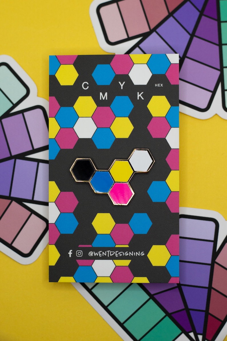 May include: A black card with a colorful hexagonal pattern and the letters CMYK and HEX. A gold-rimmed pin with black, blue, pink, and white hexagons is attached. The card has social media icons and the text "@WENTDESIGNING".