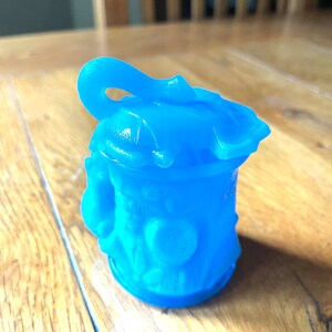 Pode incluir: Uma pequena figura de uma casa impressa em 3D de cor azul claro com um telhado curvo e um design detalhado. A casa tem uma pequena porta e janelas.