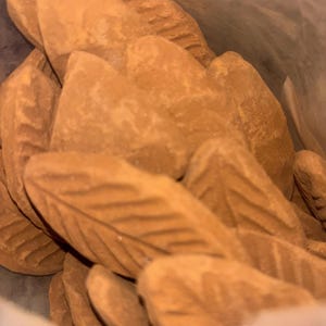 May include: Close-up shot of several light brown, leaf-shaped items, each with intricate vein detailing. The objects seem to be made of a solid material, possibly for decoration or food. The image focuses on the texture and shape of the items.