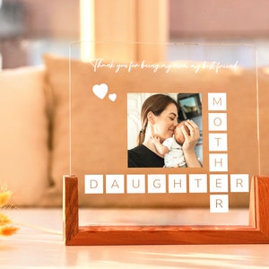 May include: A clear acrylic photo display with a wooden base. The display features a photo of a mother and baby, with the words "Thank you for being my mom my best friend" and the words "MOTHER DAUGHTER" in a crossword style.