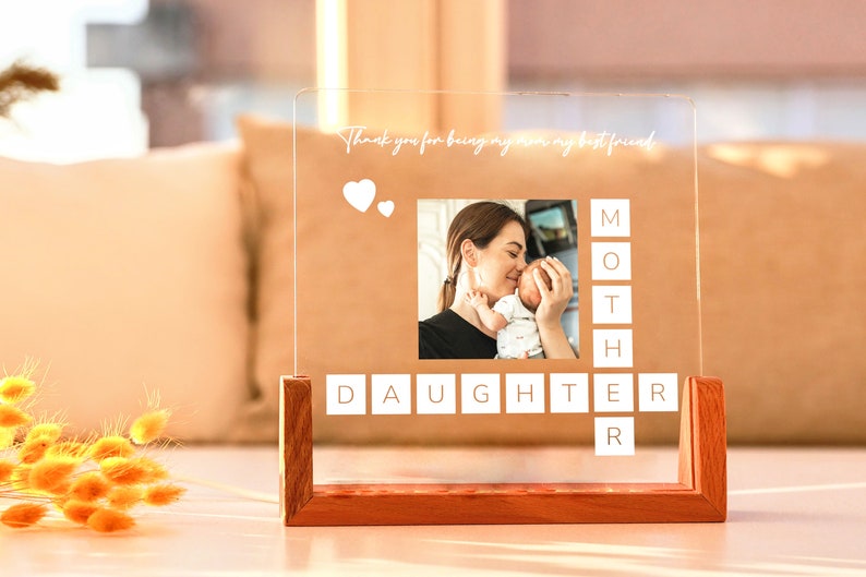 May include: A clear acrylic photo display with a wooden base. The display features a photo of a mother and baby, with the words "Thank you for being my mom my best friend" and the words "MOTHER DAUGHTER" in a crossword style.