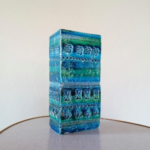 Peut inclure: Un vase rectangulaire en céramique à surface texturée. Le vase présente une palette de couleurs turquoise, sarcelle et verte. Le design comprend des motifs et des formes géométriques répétitifs. Le vase mesure environ 25 cm de haut.