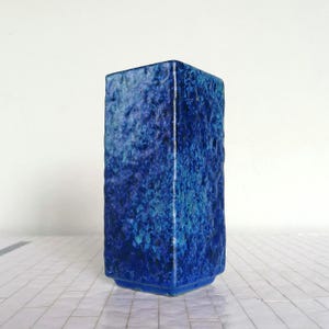 May include: A rectangular blue ceramic vase with a textured surface. The vase has a gradient of blue hues, ranging from deep indigo to lighter turquoise. The base has a slightly flared design.