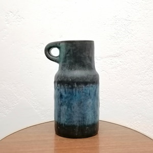 Pode incluir: Um vaso de cerâmica azul e preto com uma alça. O vaso tem um efeito de esmalte de gotejamento e é de estilo moderno de meados do século.